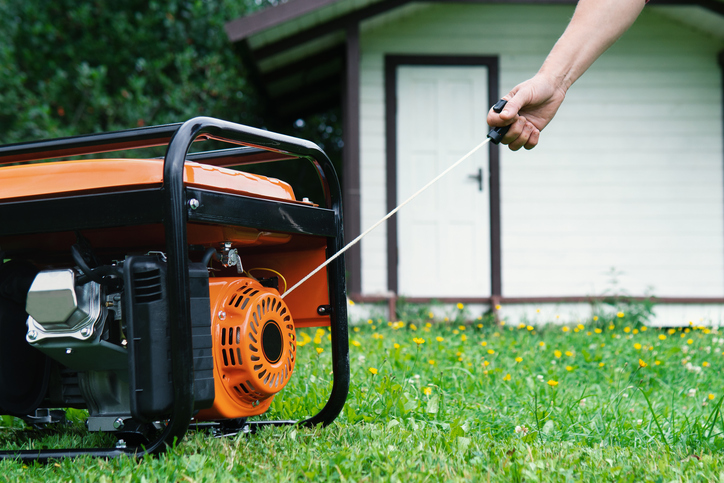 hand starts a portable electric generator standing on the grass in front of a summer house in summer evening