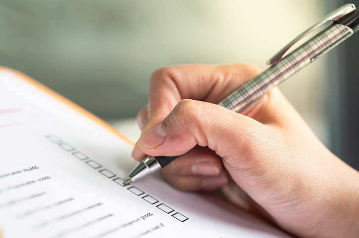 Hand holding a pen over a checklist for home generator maintenance.