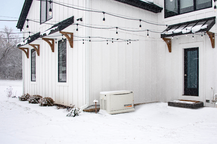Snow-covered home during a winter storm, with a visible standby generator running alongside the house.
