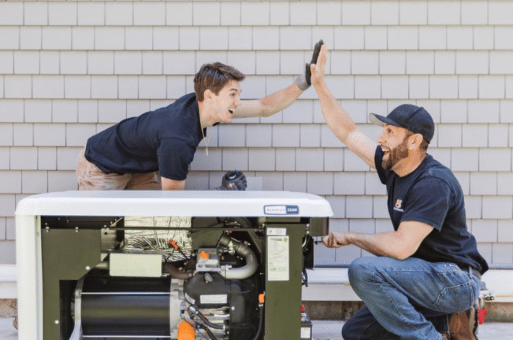 Two PE Home Generator installation techs high five over a newly installed backup home generator.