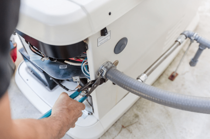 Technician tightening a hose connection on a standby home generator during installation or service.