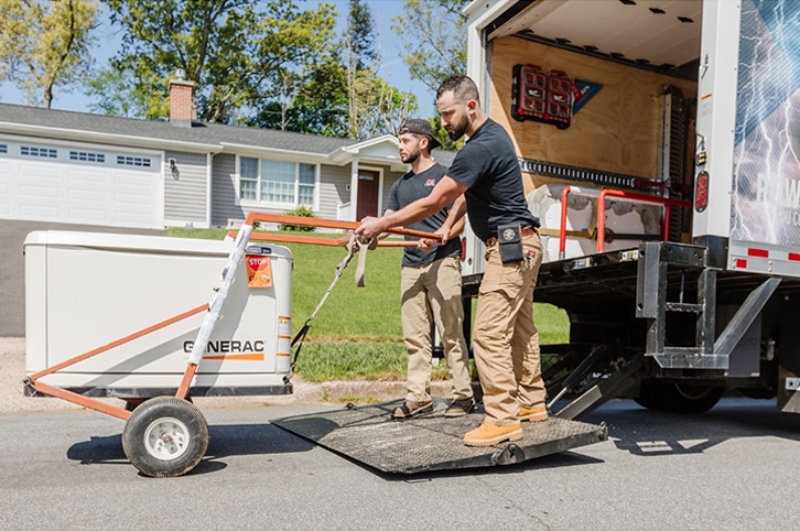 PE Home Generator technicians unloading a Generac whole-home generator from a service truck at a home on a bright, sunny day.