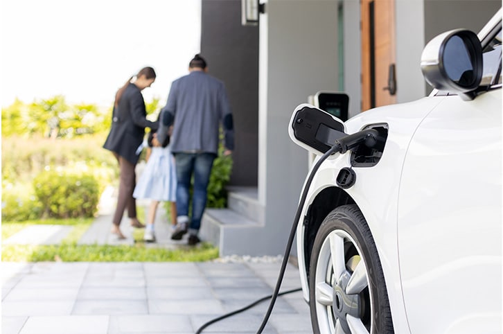 Electric vehicle charging in a home's driveway as the family walks inside.