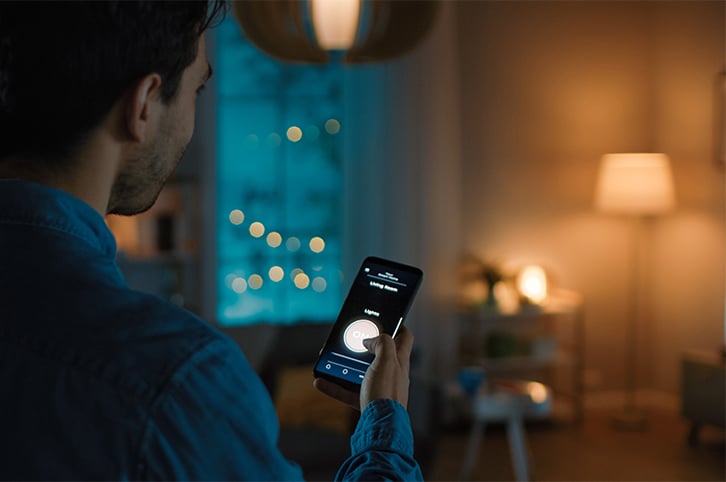 Man holding a smartphone displaying an app that controls the lighting in his house.
